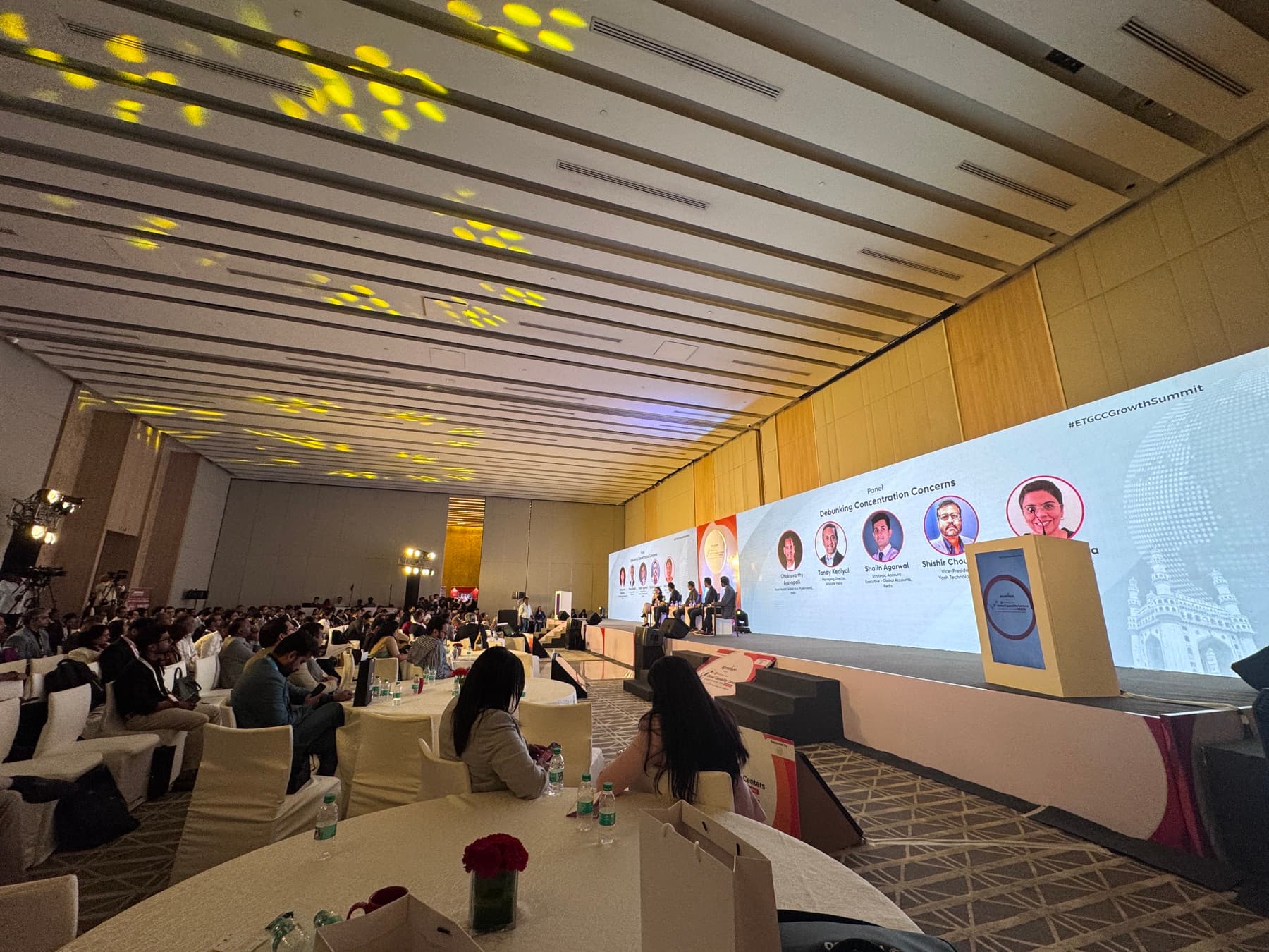 A packed growth summit hall with a panel on stage and large screens.