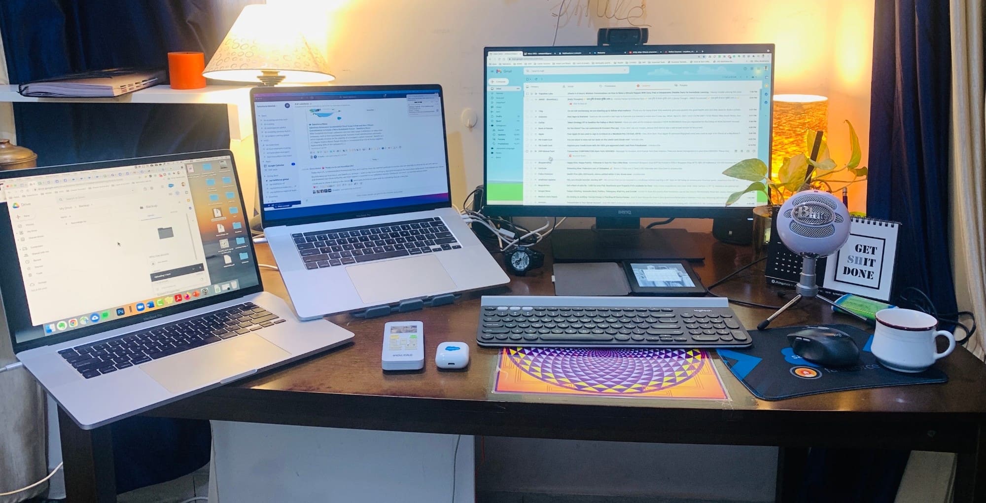 A multi-screen work desk with two laptops, a monitor, a keyboard and a microphone.