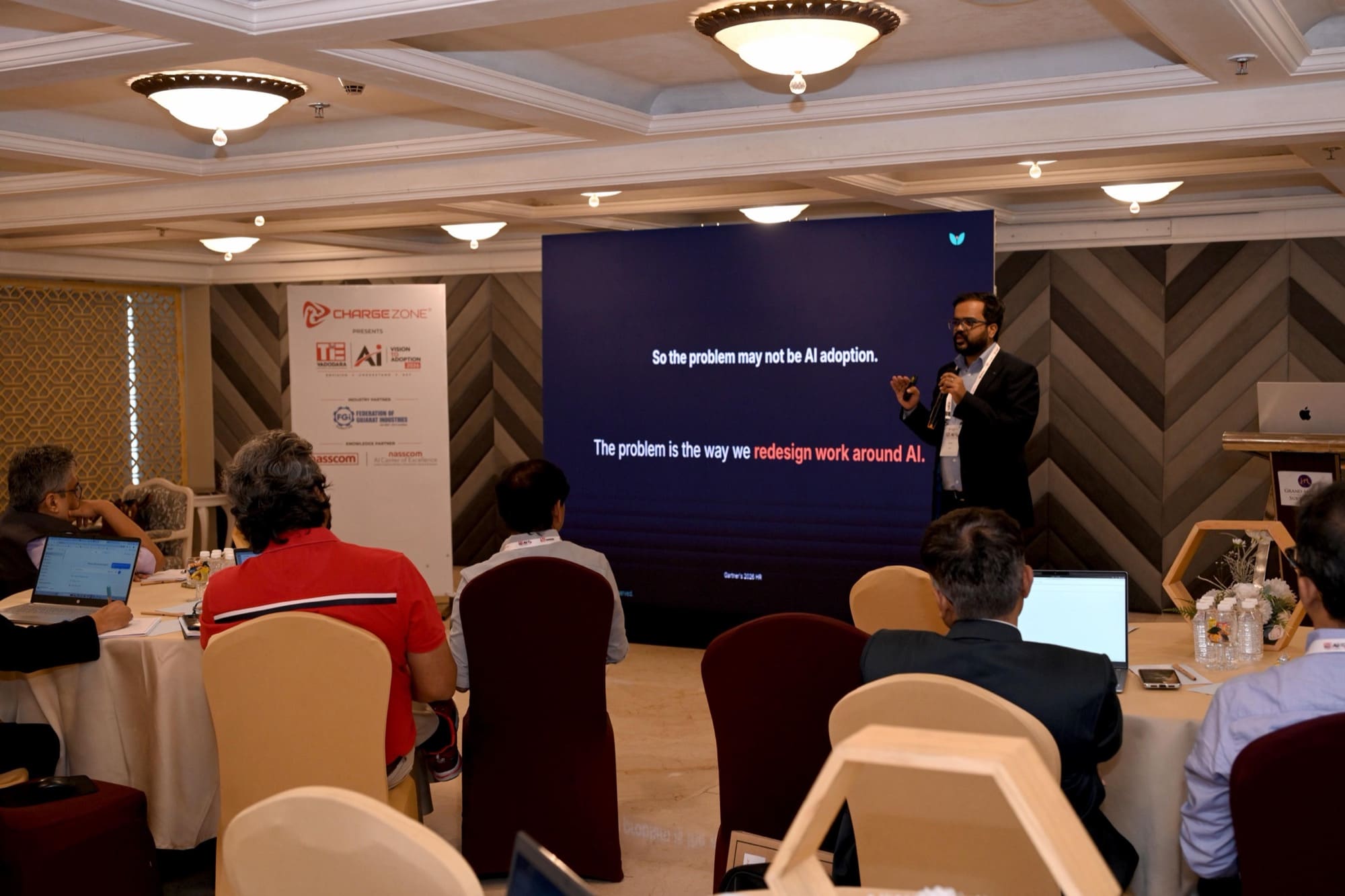 Amit presenting to a seated room of professionals beside a large screen.